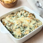 Creamy spinach artichoke dip baked in a white square dish with a golden cheesy top, served with tortilla chips.