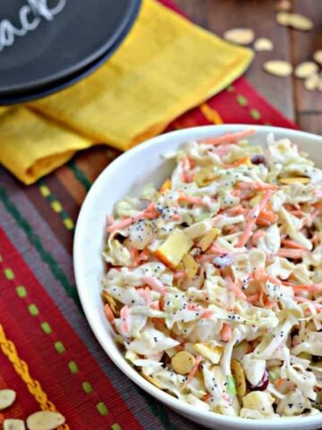white bowl of coleslaw with apples, cranberries and almonds on festive placemat