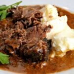 The MOST Amazing Slow Cooker Pot Roast white plate with slow cooker pot roast, gravy and mashed potatoes