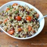 Overhead shot of Israeli couscous, grape tomatoes in white bowl with spoon