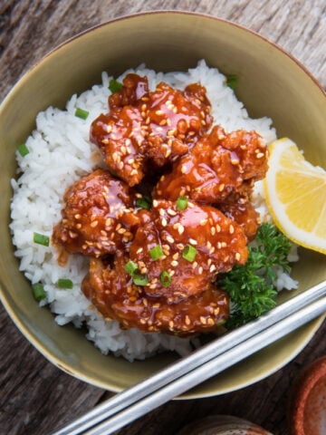 sesame chicken with toasted sesame seeds over white rice in a bowl