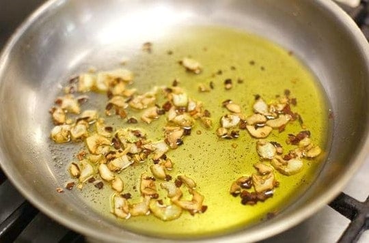 skillet with oil and thinly sliced garlic browning, red pepper flakes