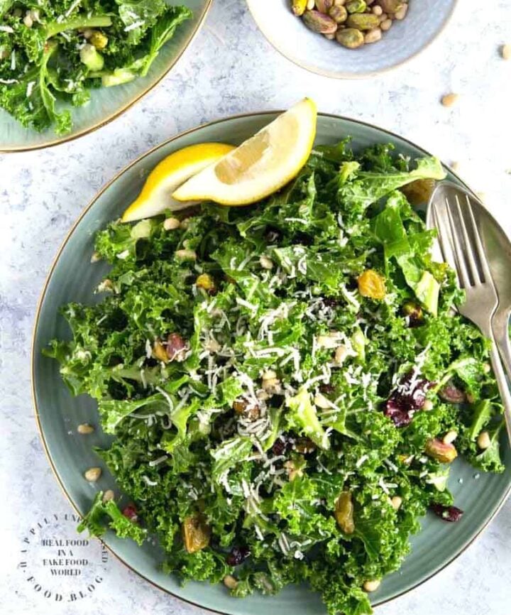 An easy lemony garlic kale salad with pistachios, pine nuts, dried cranberries topped with shaved parmesan cheese #newyearsresolution #kale #salad #healthy #happilyunprocessed
