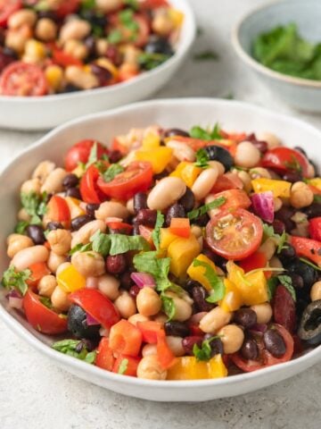 Summer four bean salad with black beans, kidney beans, cannellini beans, chickpeas, tomatoes, peppers, olives, red onion, and fresh herbs.