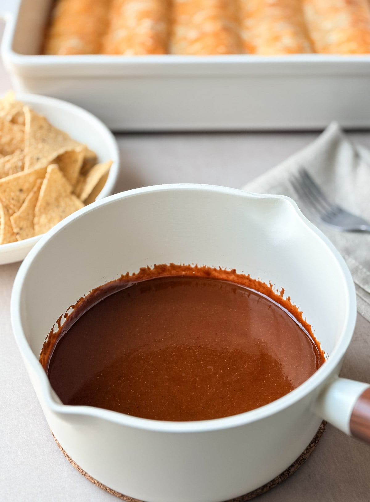 White sauce pan with homemade red enchilada sauce on a table with other side dishes