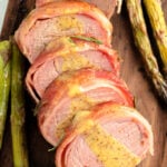 Bacon Wrapped Pork Tenderloin sliced on a cutting board drizzled in a honey dijon sauce